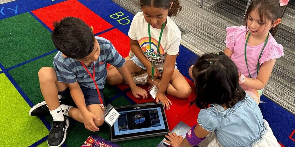 Four primary students sitting together on the carpet following the Starforce story on a tablet