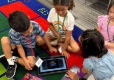 Four primary students sitting together on the carpet following the Starforce story on a tablet